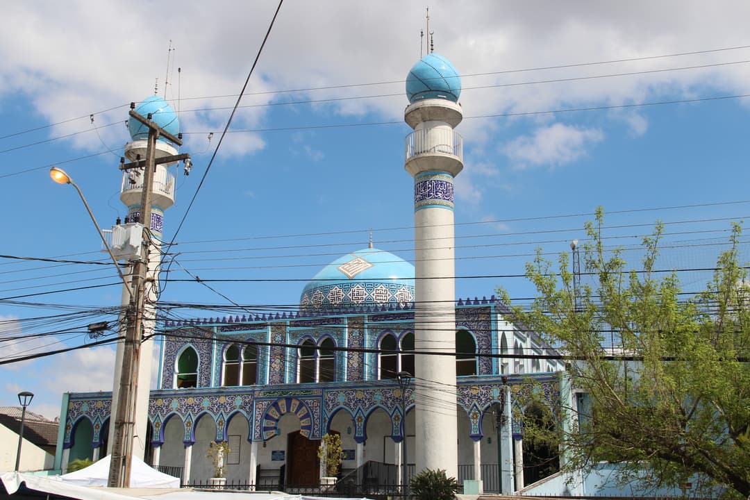 Front facade of Mesquita Brasil featuring blue domes and minarets in daylight.