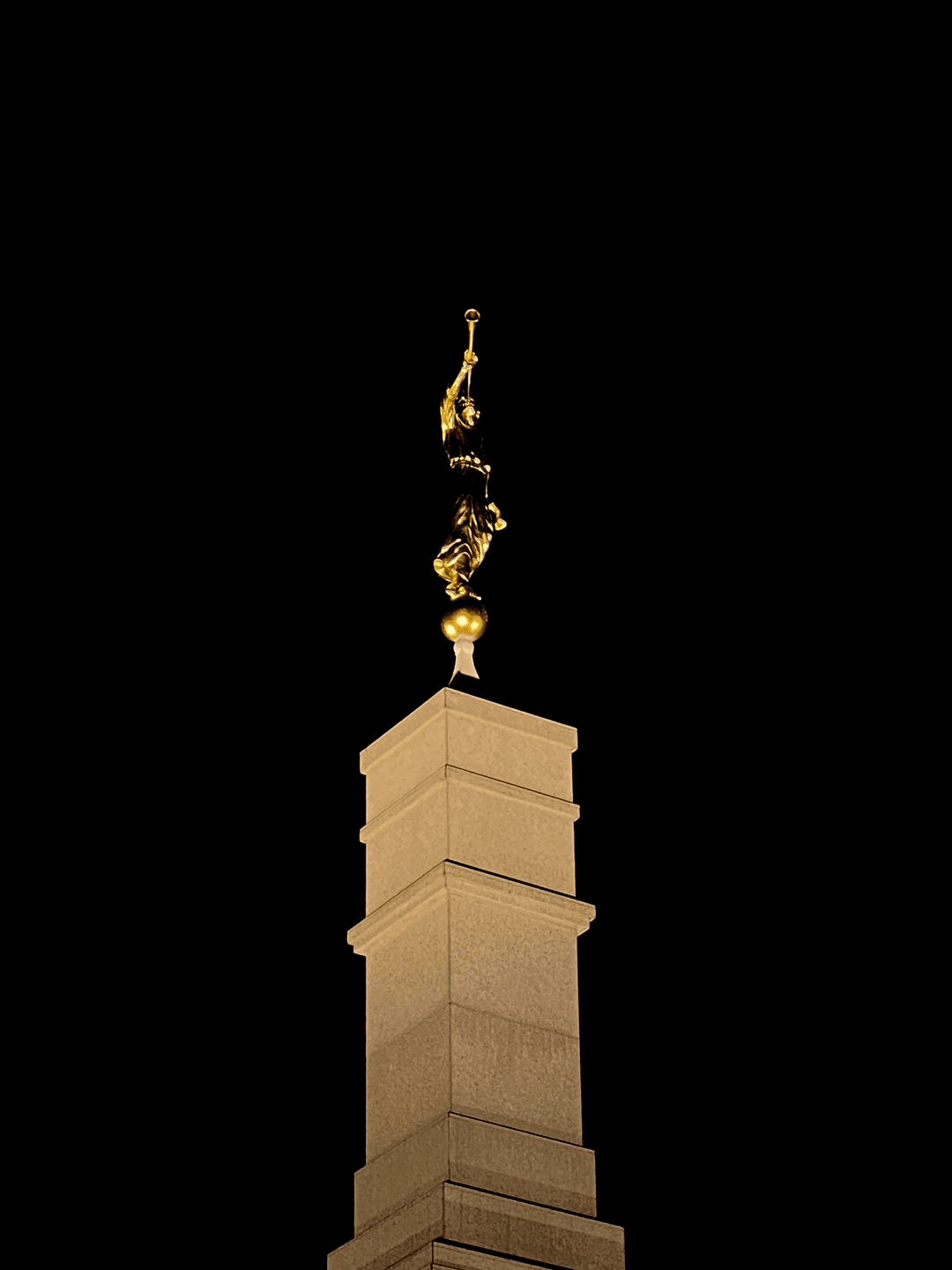 Illuminated Angel Moroni statue atop the temple spire at night.