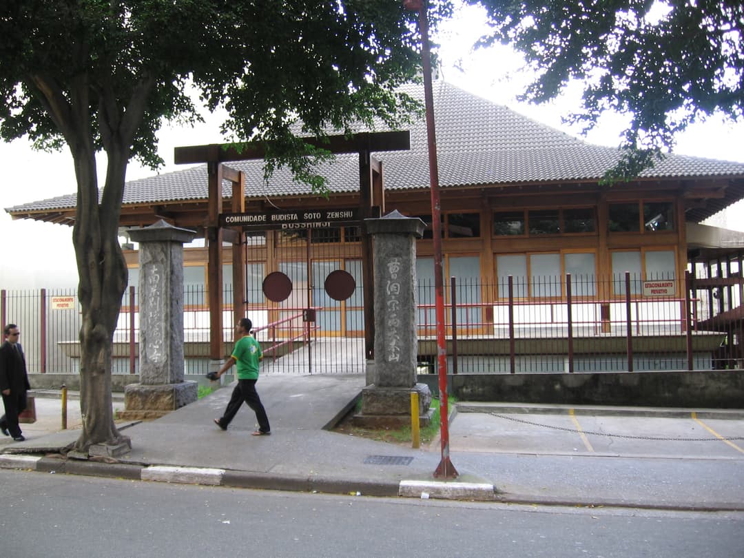 Front entrance of Templo Busshinji with wooden gate and stone pillars.