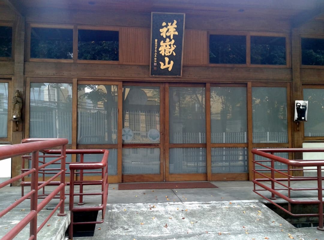 Front entrance of Templo Busshinji with calligraphy plaque and red handrails.