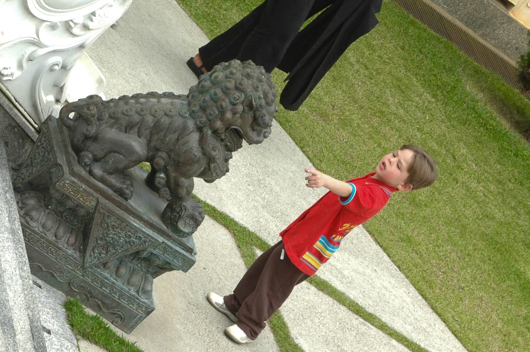 Boy pointing at a bronze guardian lion statue on the temple grounds.