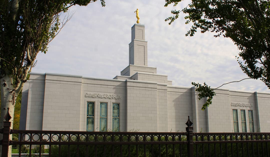 Montreal Quebec Temple exterior, with Angel Moroni, framed by trees and fence.