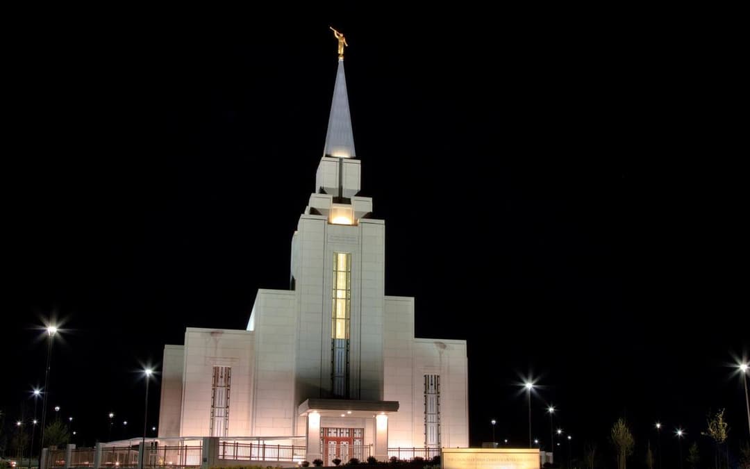 The illuminated front facade and spire of the temple at night.