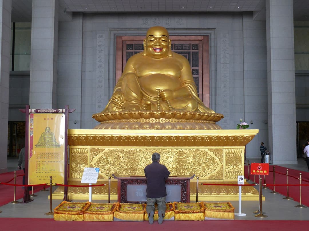 Golden Maitreya Buddha statue and kneeling worshiper inside Famen Temple
