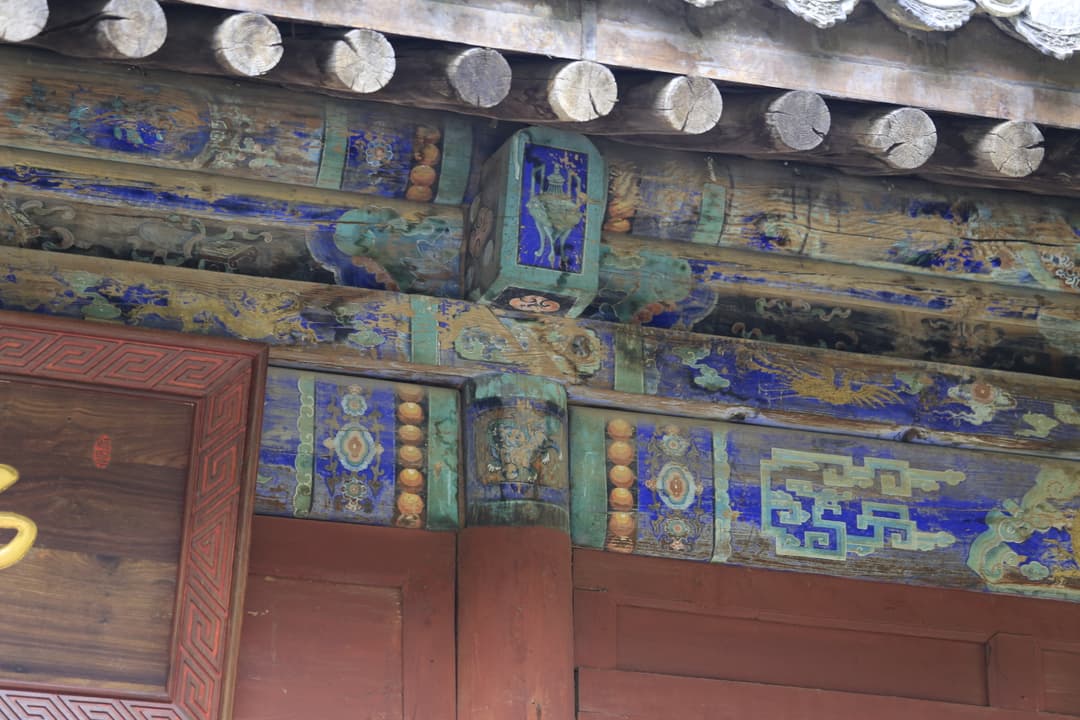 Detail of polychrome painted wooden beams and rafters under the eaves.