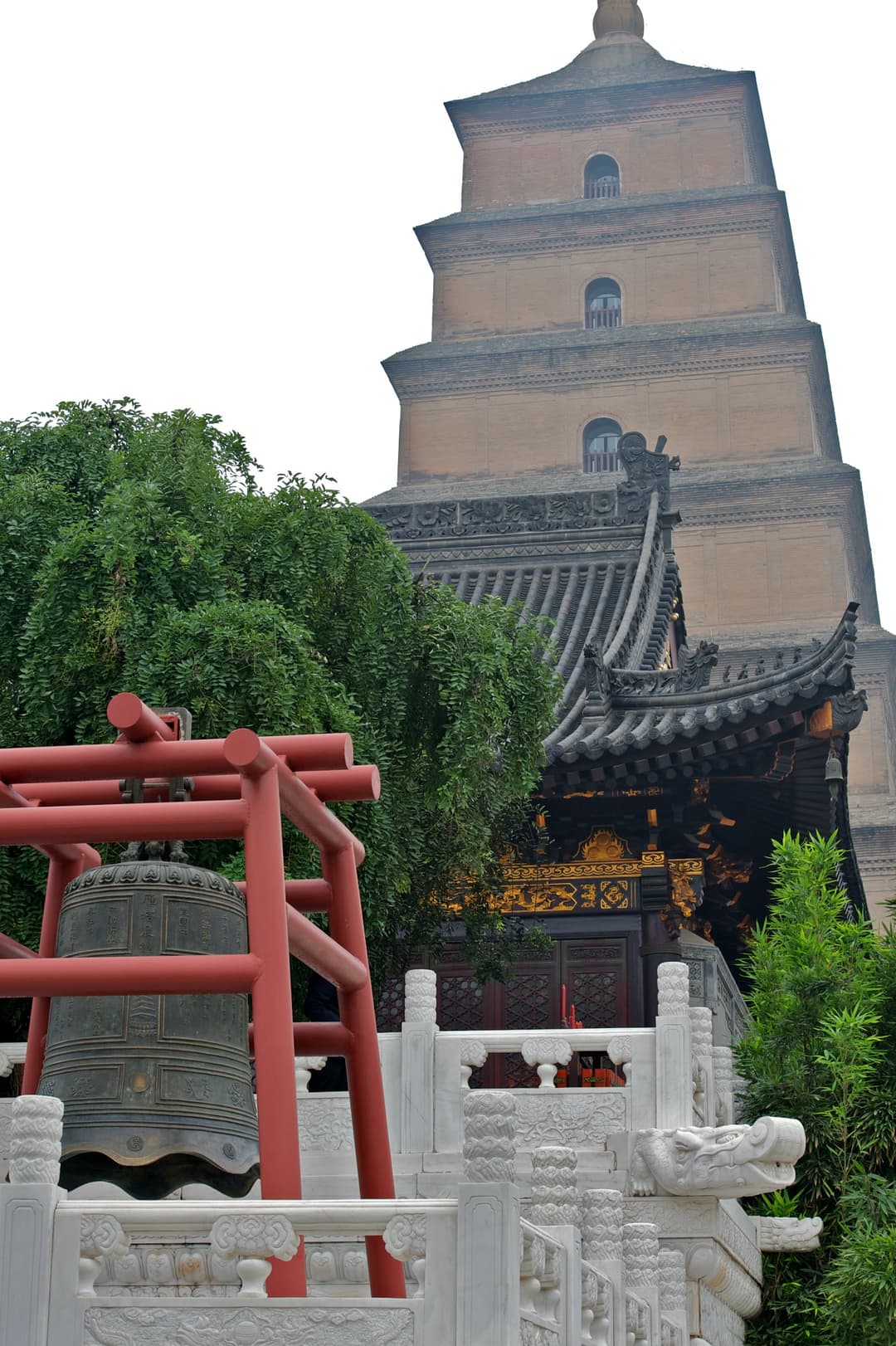 Giant Wild Goose Pagoda rising behind a bronze bell and temple eaves.