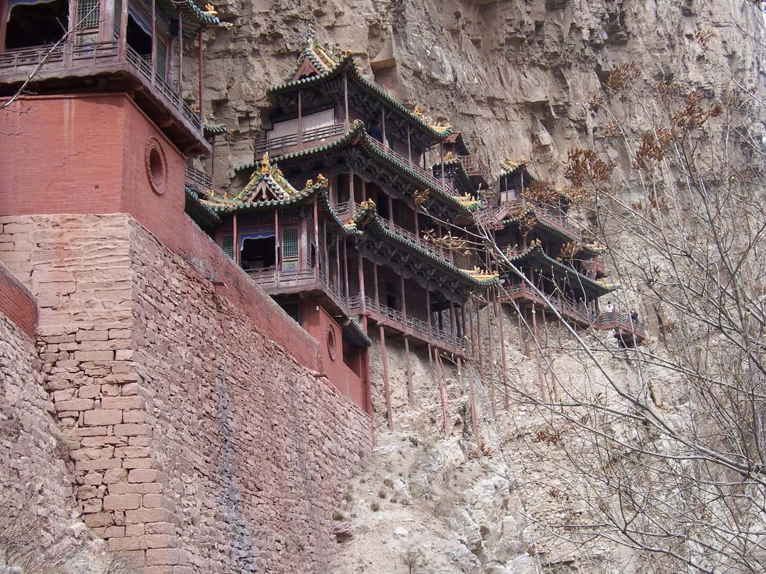 Low-angle view of timber pavilions built into the sheer cliff face.
