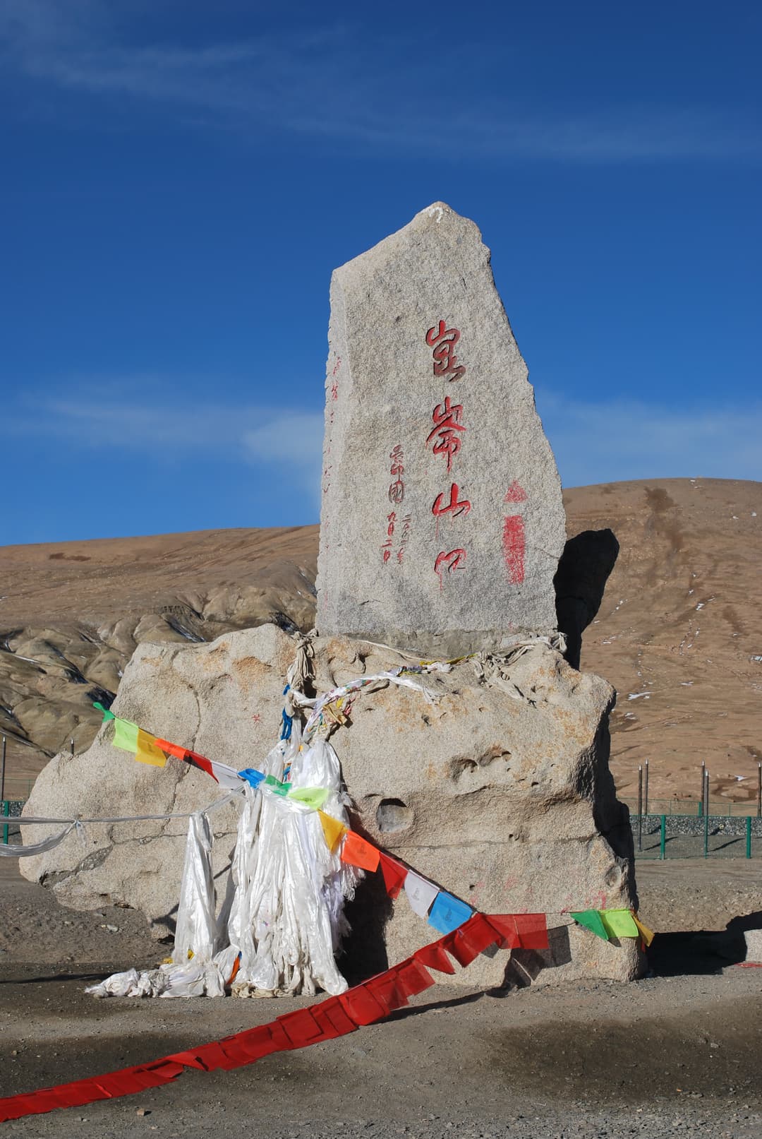 Stone marker at Kunlun Mountain Pass adorned with prayer flags.
