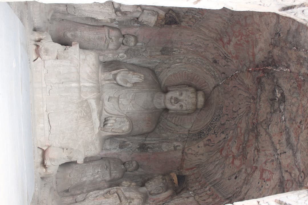 Interior view of a rock-cut niche featuring a central seated Buddha.