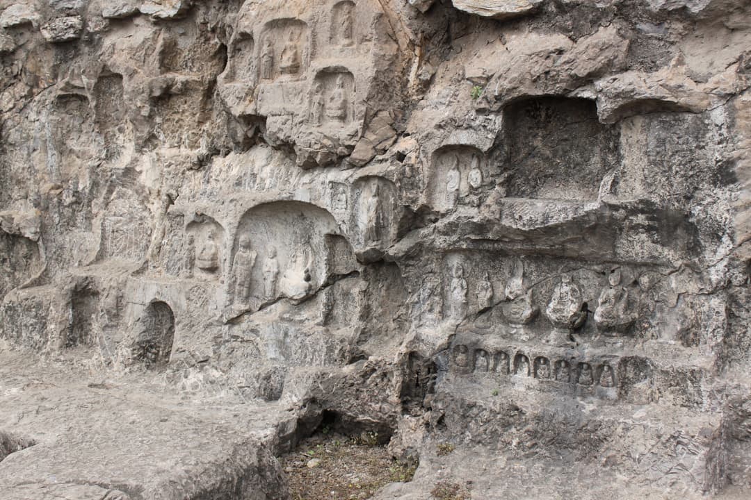 Weathered limestone cliff with small carved Buddhist niches and relief figures.