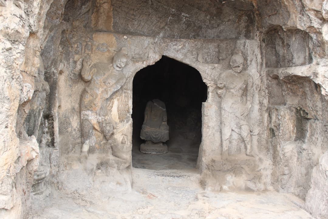 Front entrance of a rock-cut cave shrine flanked by carved guardian figures.