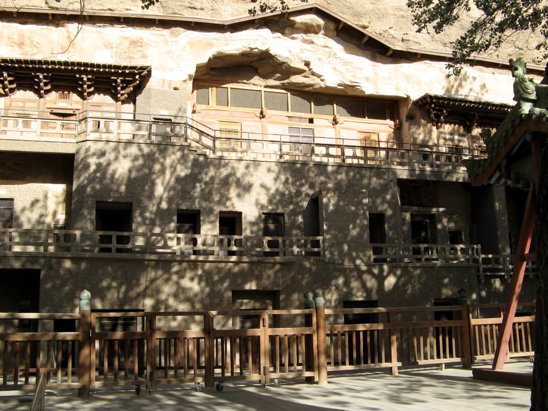 Front view of the multi-tiered Mogao Cave facade with dappled tree shadows.