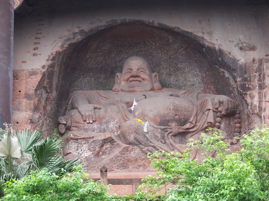 Rock-cut carving of the Laughing Buddha in a cliffside niche.
