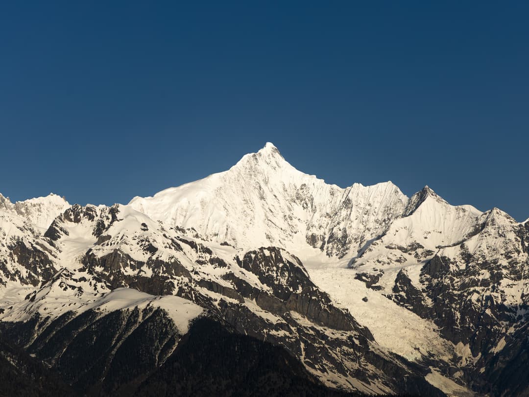 Daytime view of Mount Kawagarbo's snow-capped peak against a clear sky.