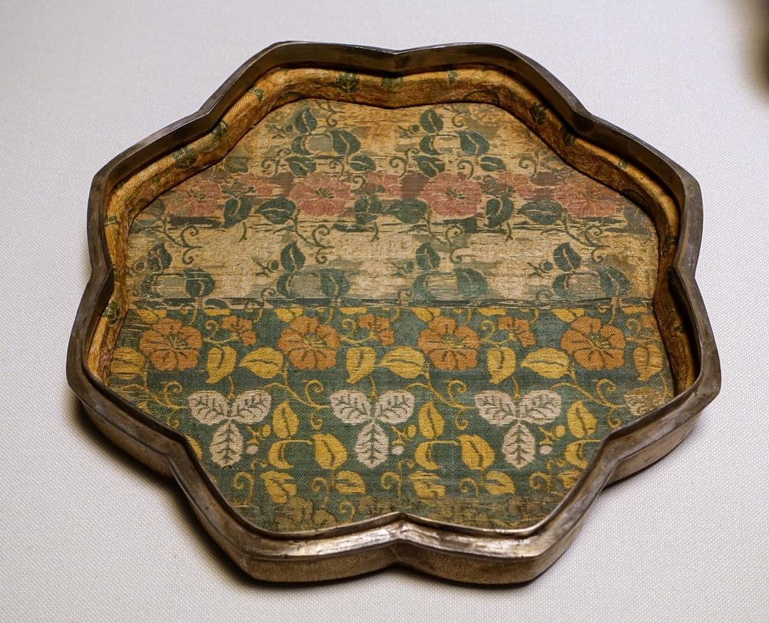 Antique lobed tray lined with patterned floral silk brocade on display
