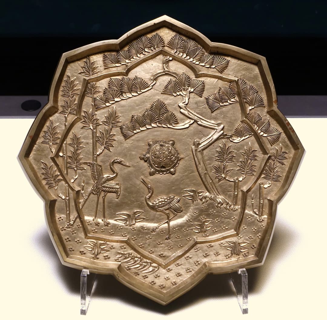 Exhibited lobed metal dish depicting cranes, a tortoise, and pine trees