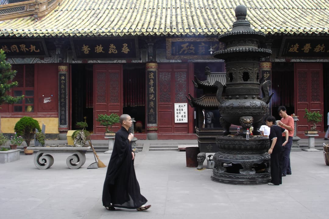 A monk walks past a large incense burner in a Mount Putuo temple courtyard.