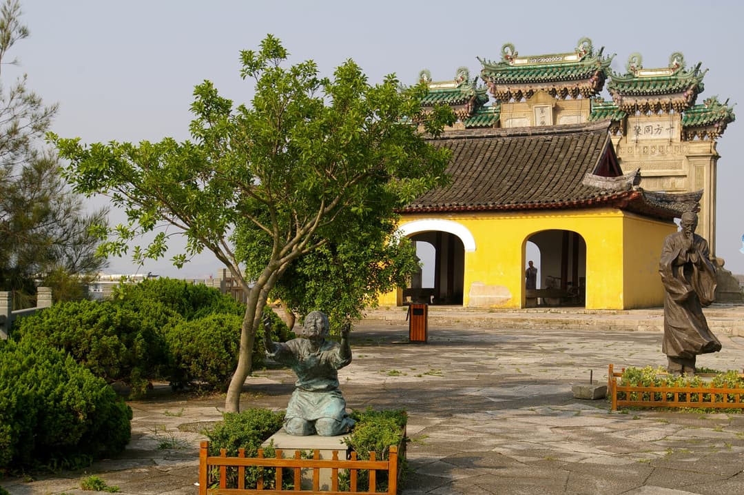 Temple courtyard with bronze statues, yellow pavilion, and ornate archway.