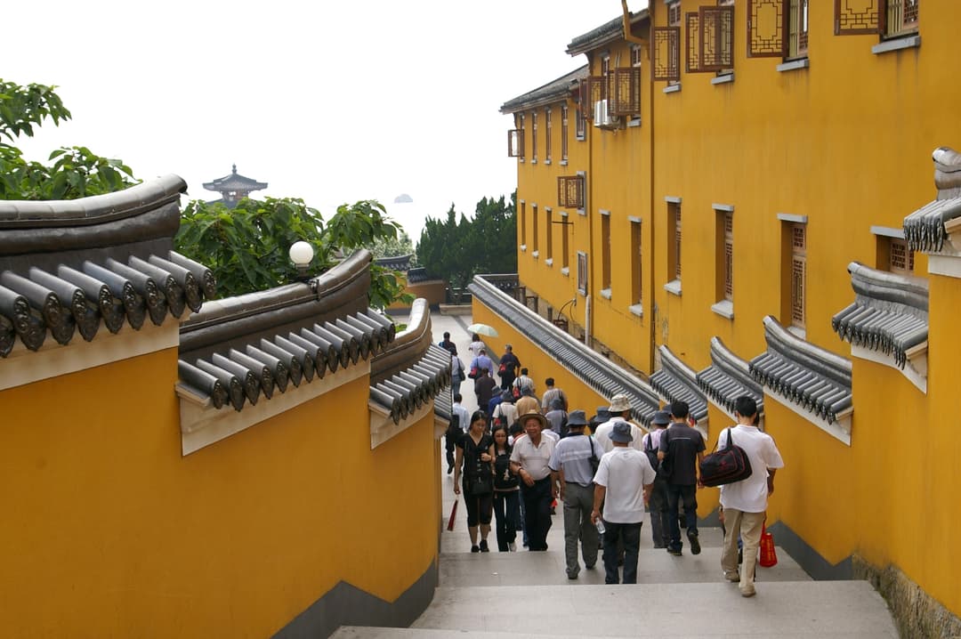 High-angle view of visitors walking down stairs between yellow temple walls.