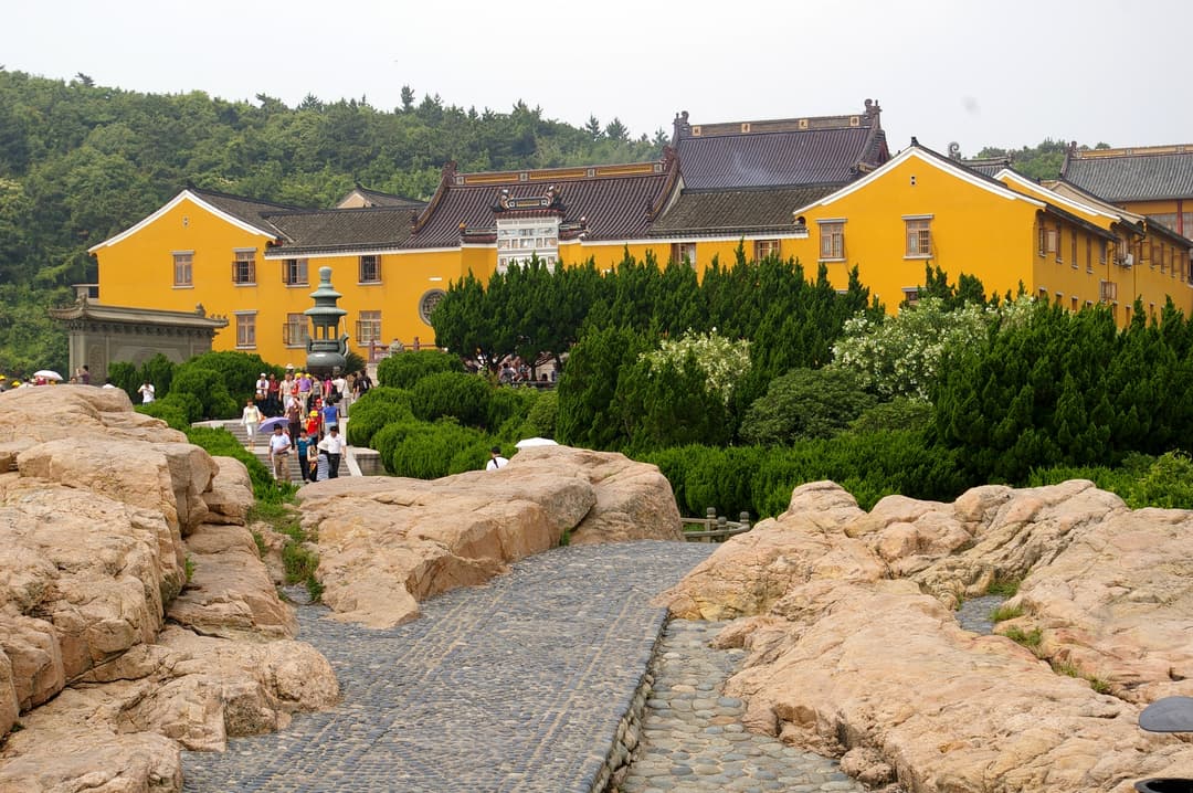 Wide-angle exterior view of yellow-walled temple complex and rocky stone path.