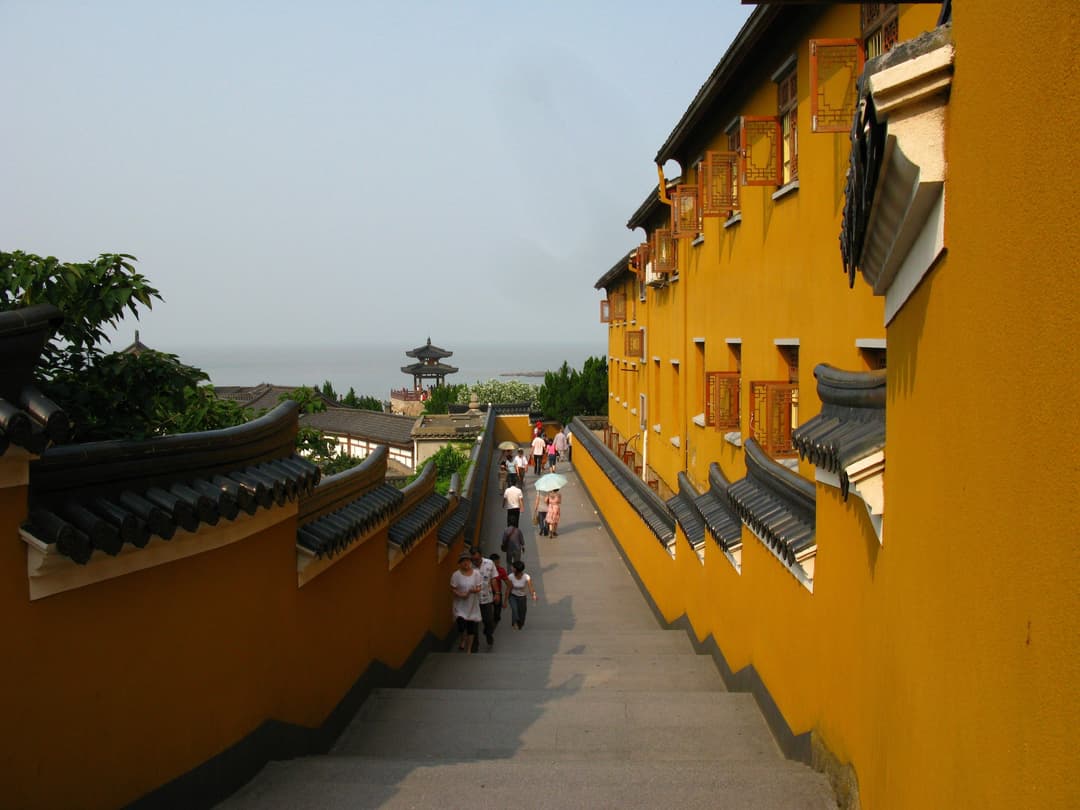 Stone staircase flanked by yellow temple walls leading toward the sea.