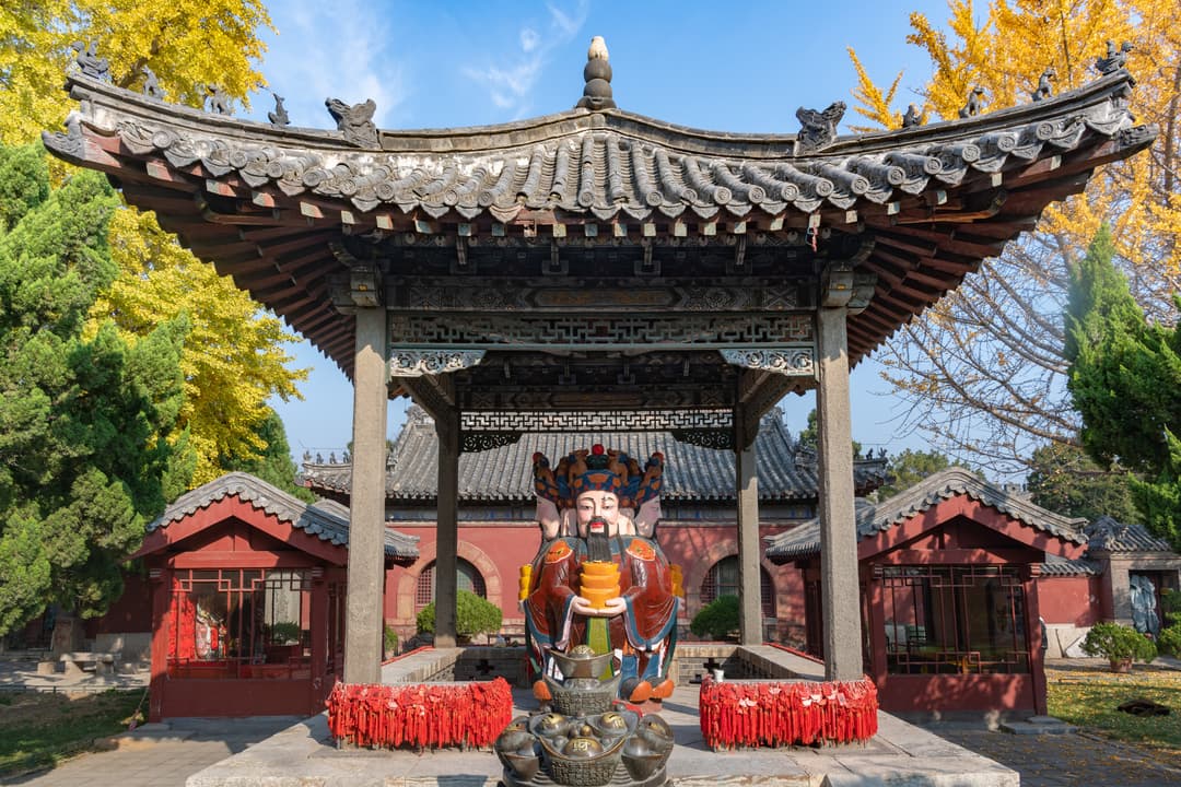 Front view of an open pavilion housing a multi-faced deity statue in autumn.