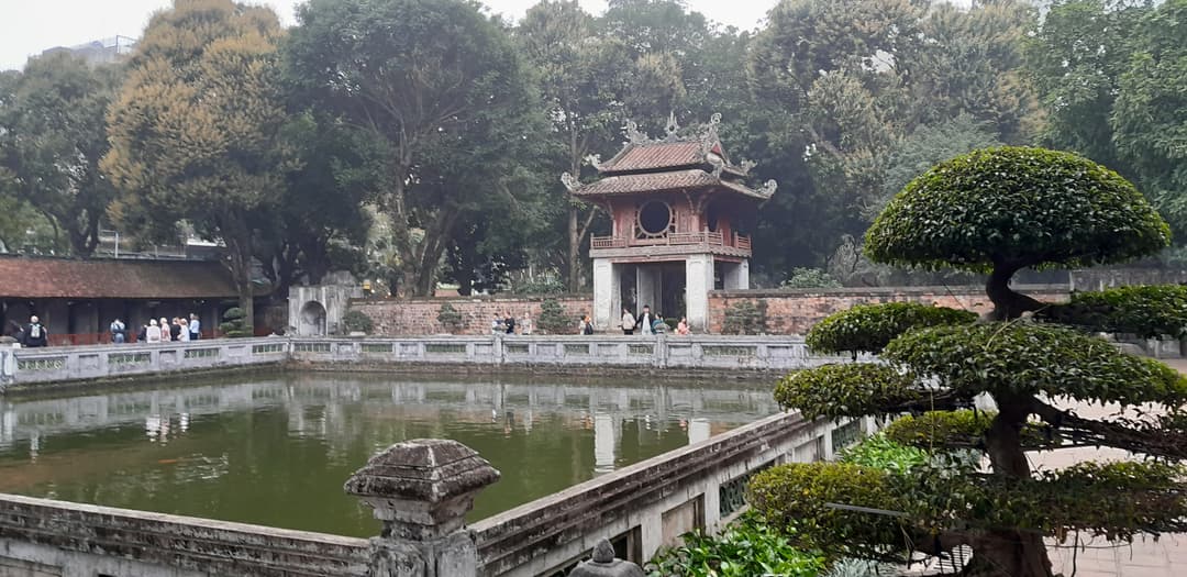 Pavilion and square reflecting pond bordered by stone railings and trees.