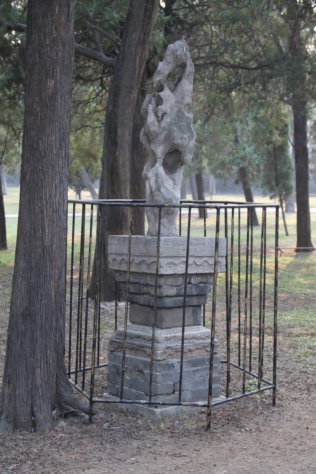 A scholar's stone on a carved pedestal enclosed in a protective metal cage.