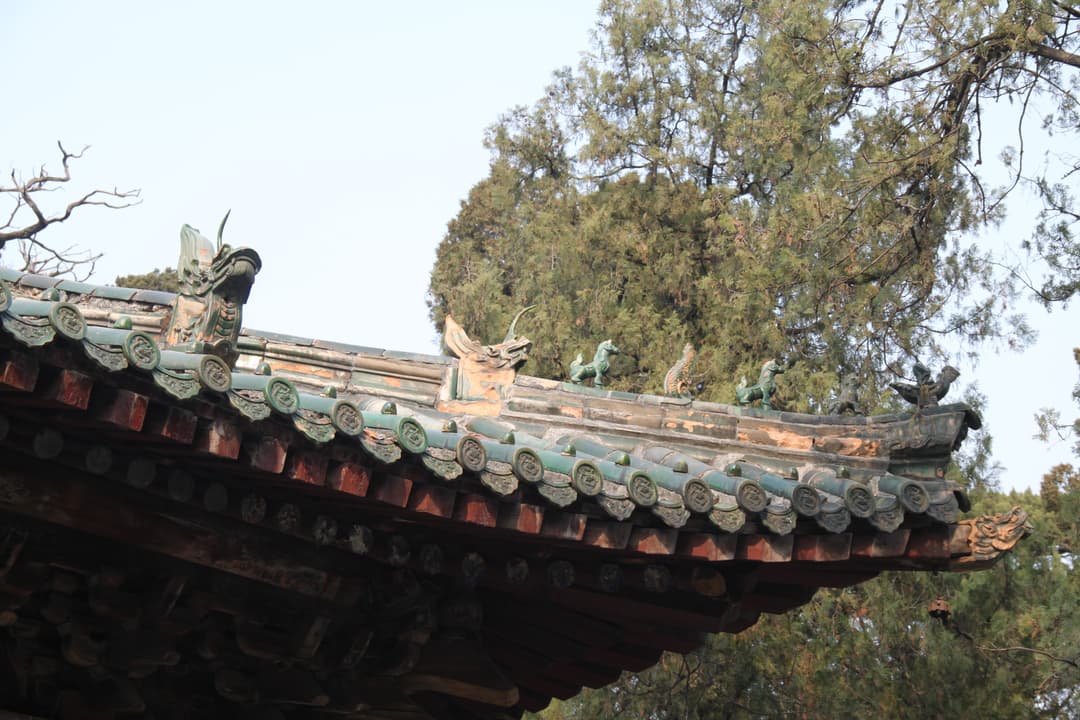 Low-angle view of green-glazed roof tiles and decorative roof ridge beasts.