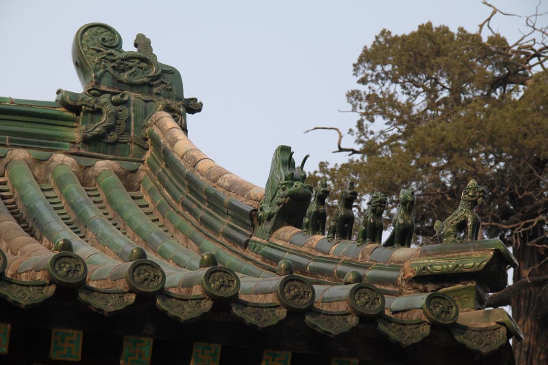 Low-angle close-up of green glazed tiles and roof ridge beasts in daylight.