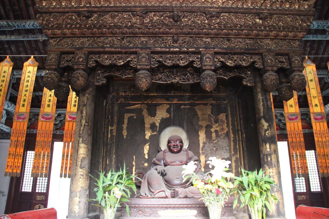Statue of Maitreya Buddha under an ornate carved wooden shrine, interior view