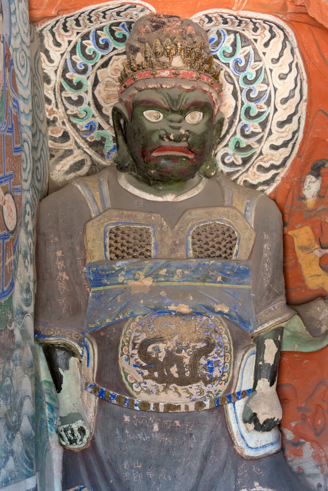 Rock-cut green-faced guardian deity sculpture at Yungang Grottoes.