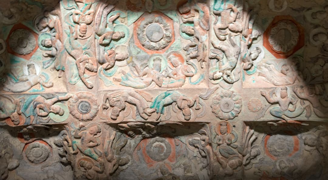 Intricate stone ceiling reliefs featuring flying apsaras at Yungang Grottoes.