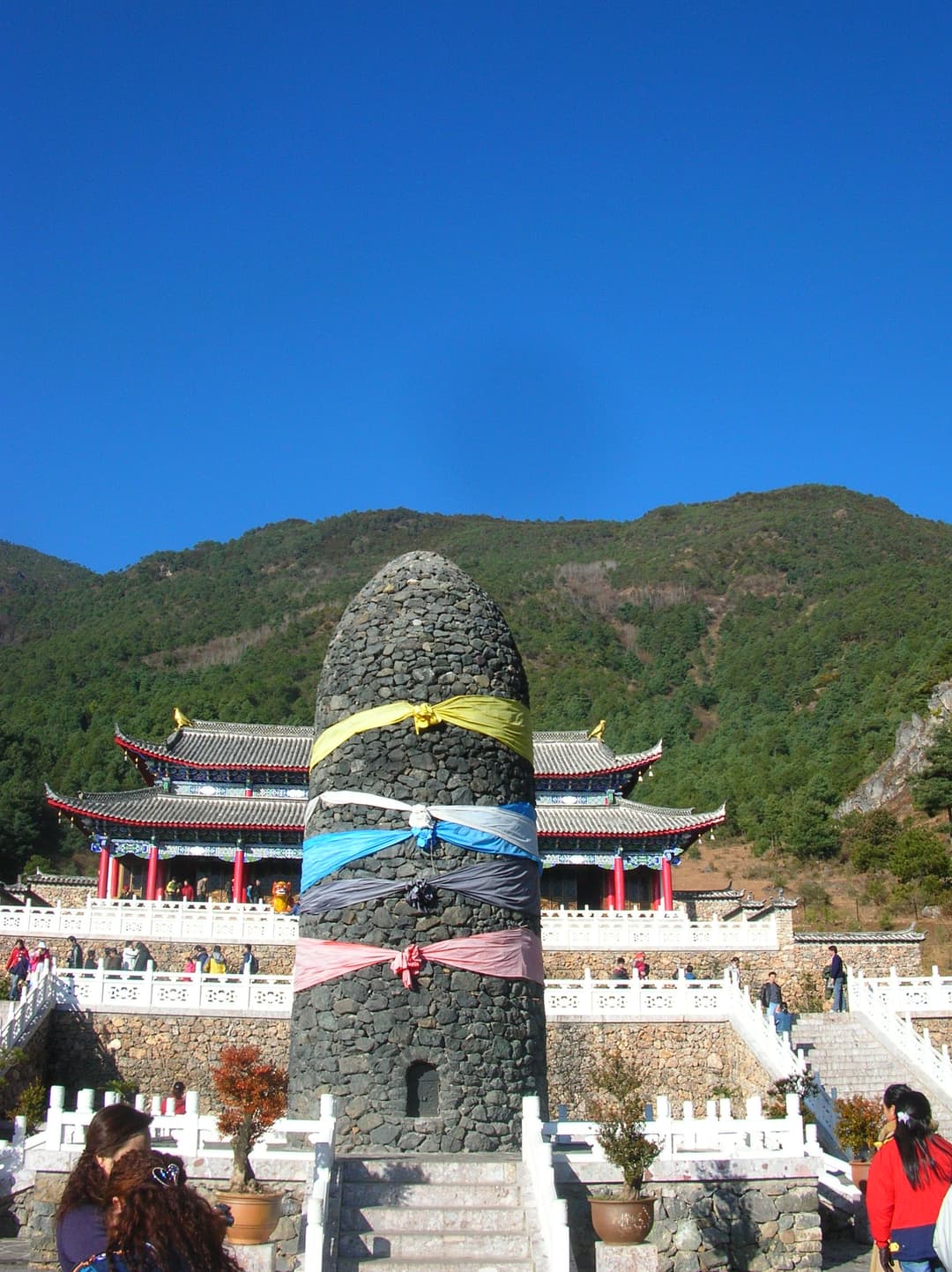 A sacred stone pillar tied with prayer scarves in front of a Naxi temple.