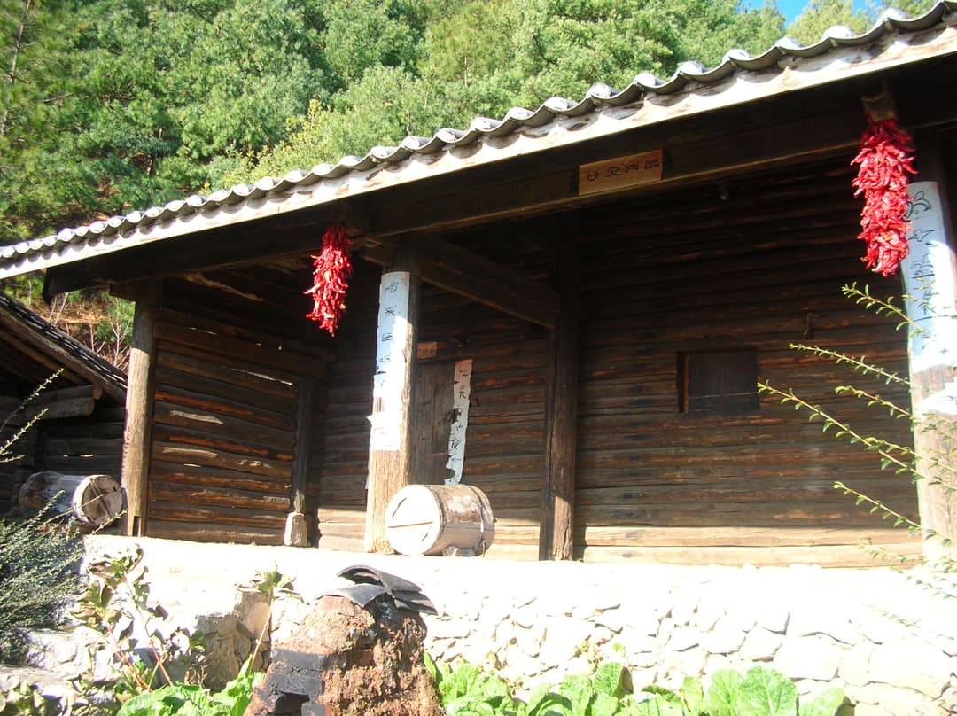 Sunlit exterior of a traditional Naxi log cabin with hanging red peppers.
