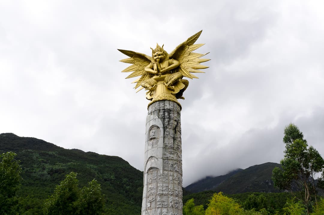 Low-angle view of a golden Garuda statue atop a carved stone pillar.