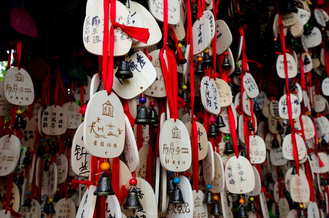 Wooden Dongba wish plaques with small bells hanging on red ribbons.