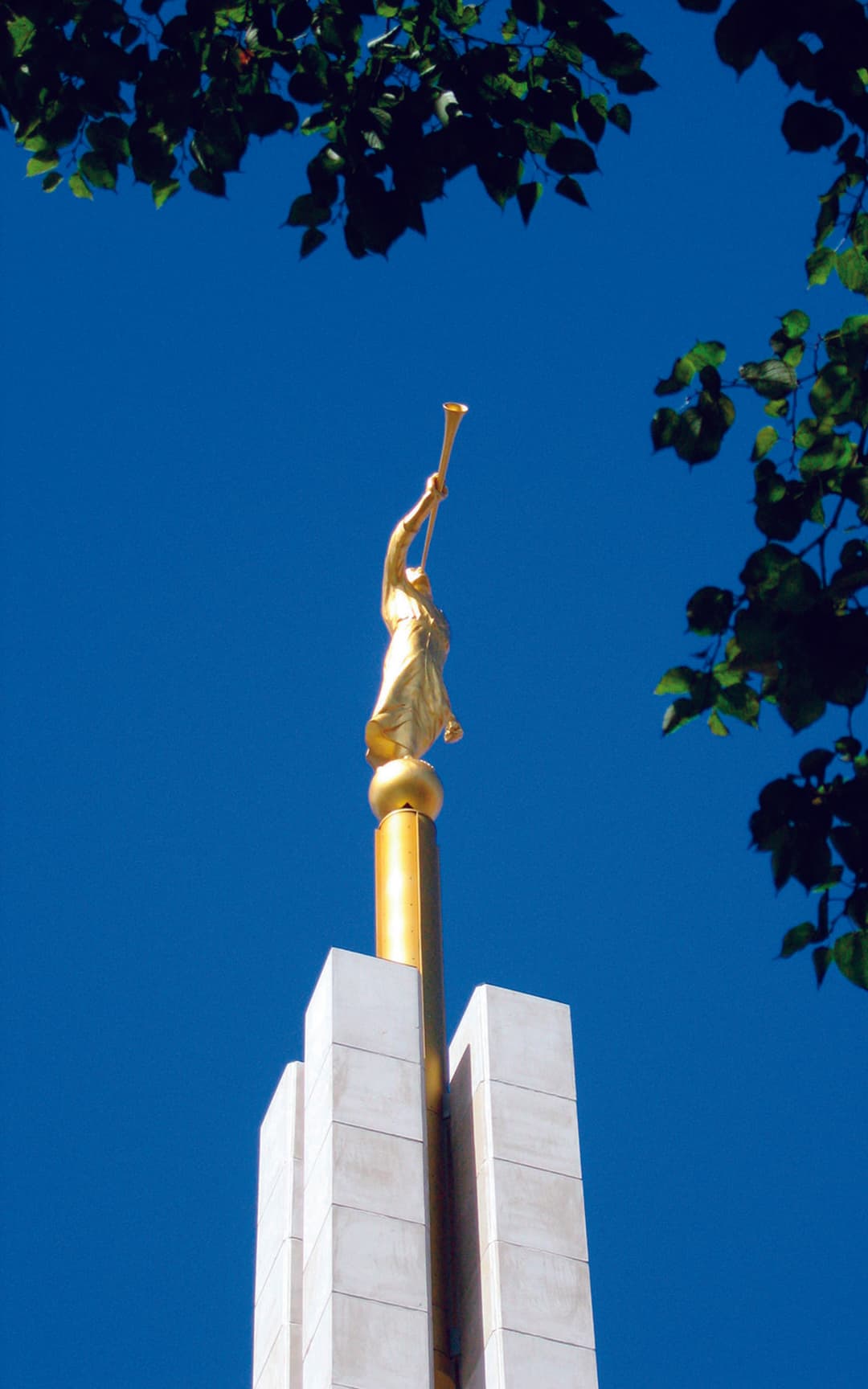 Low-angle view of the golden Angel Moroni statue against a clear blue sky.