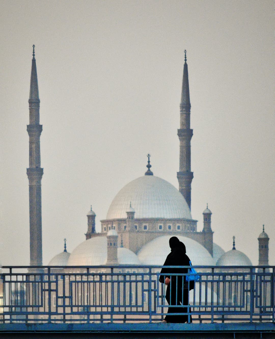 Kuppeln und Minarette der Muhammad-Ali-Moschee hinter einer Frau auf einer Brücke.
