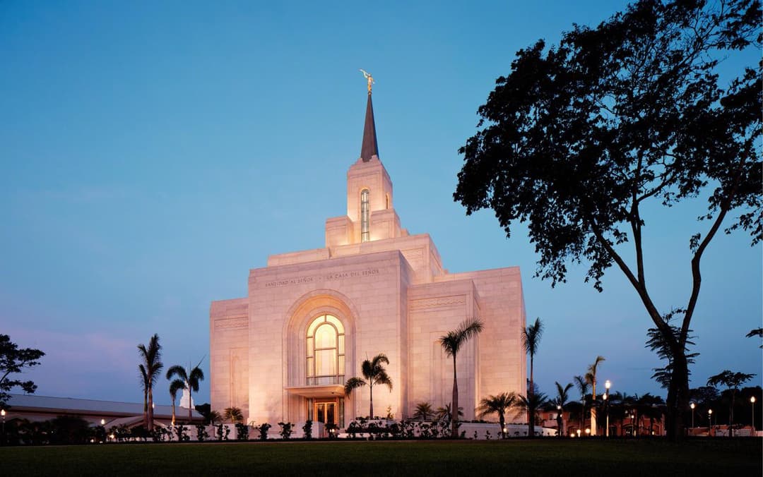Illuminated front facade of the San Salvador El Salvador Temple at twilight.