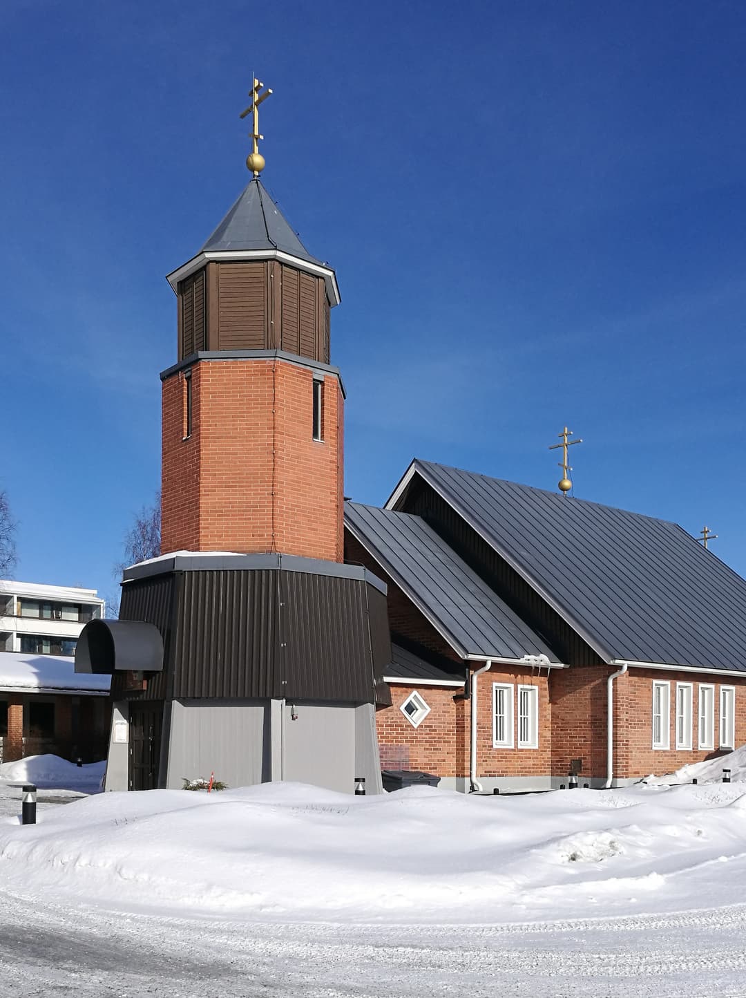 Exterior view of a brick church with a steeple, cross, and metal roof.