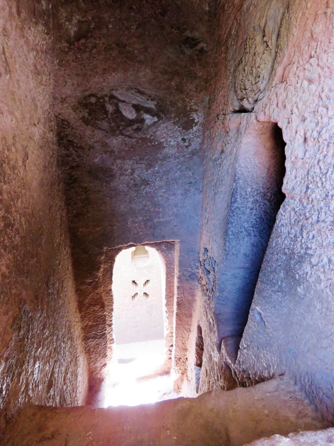 Looking down a rock-hewn passage toward an arched doorway, Lalibela