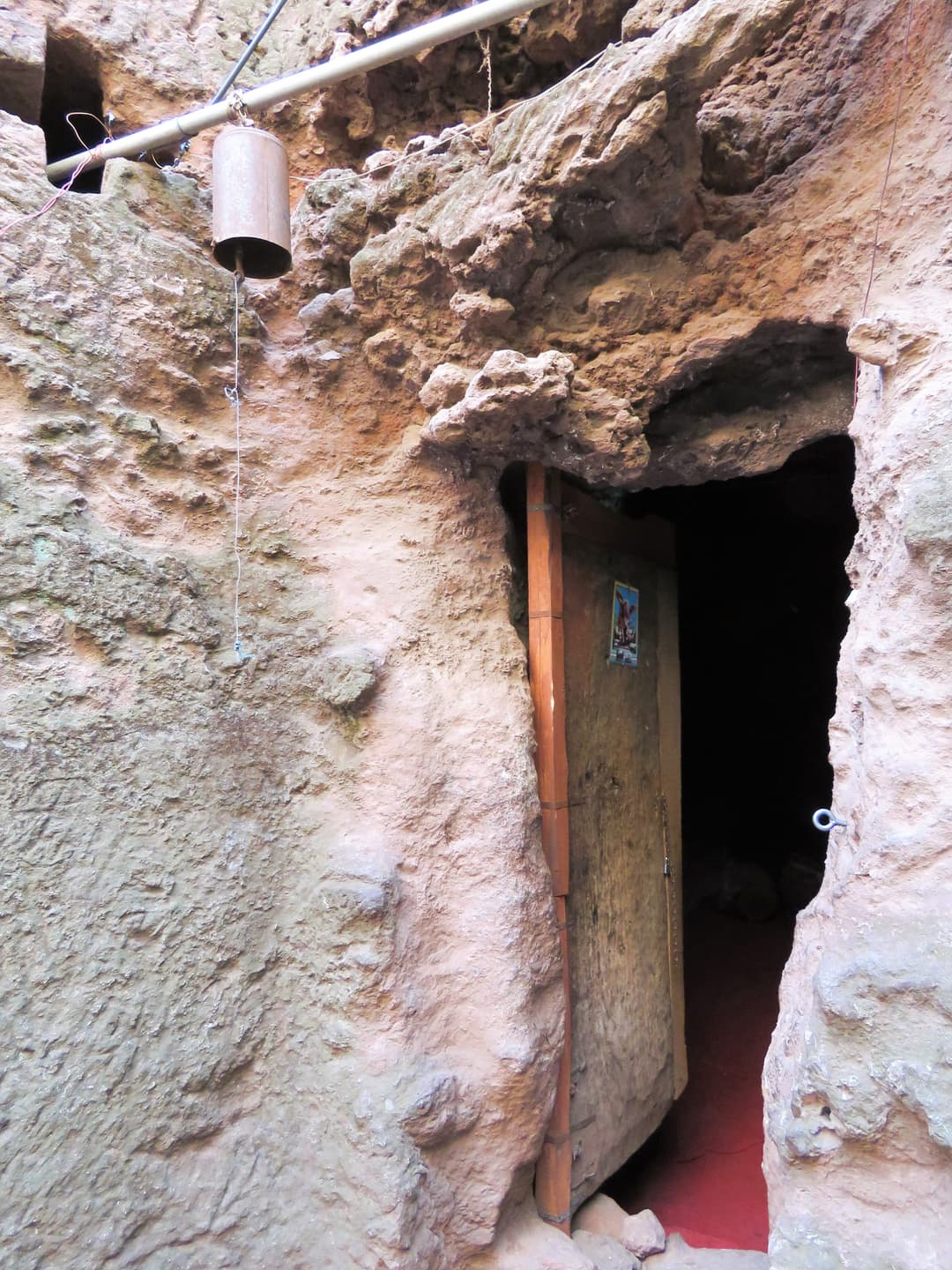 Rock-hewn entrance with a wooden door and hanging bell, Lalibela