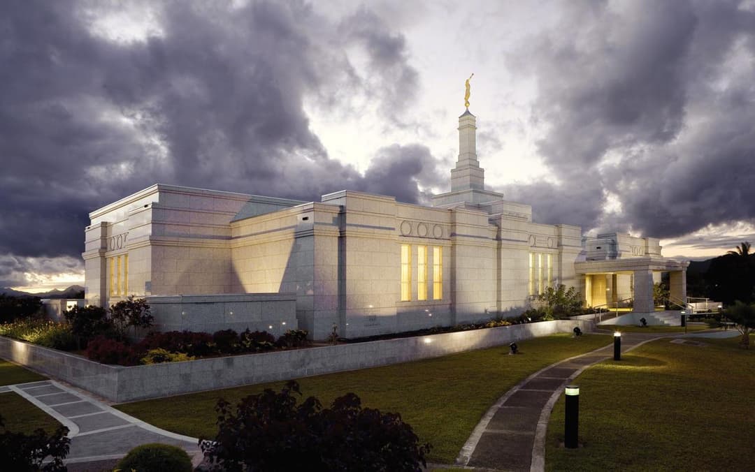 Exterior of the Suva Fiji Temple illuminated at twilight under dramatic clouds.