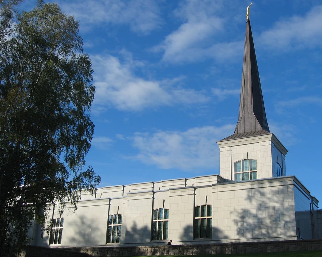 Helsinki Finland Temple exterior with spire, Angel Moroni, and tree.