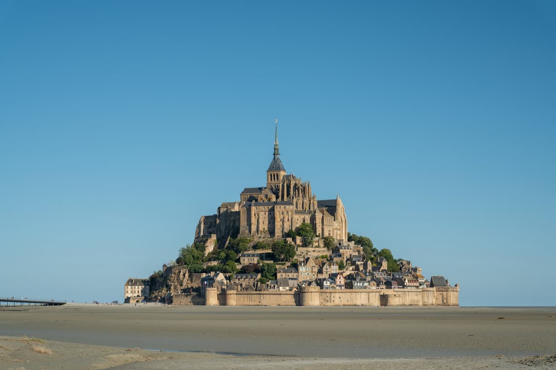 Wide view of Mont-Saint-Michel across the tidal flats under a clear sky