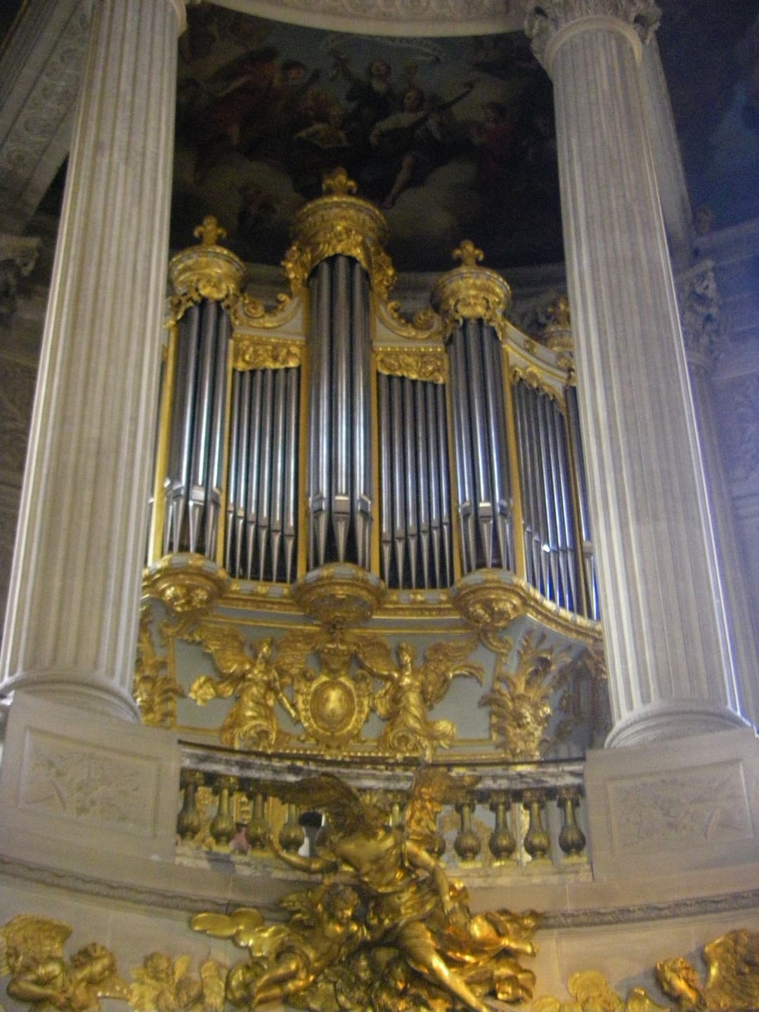 Gilded pipe organ framed by columns in the Royal Chapel of Versailles.