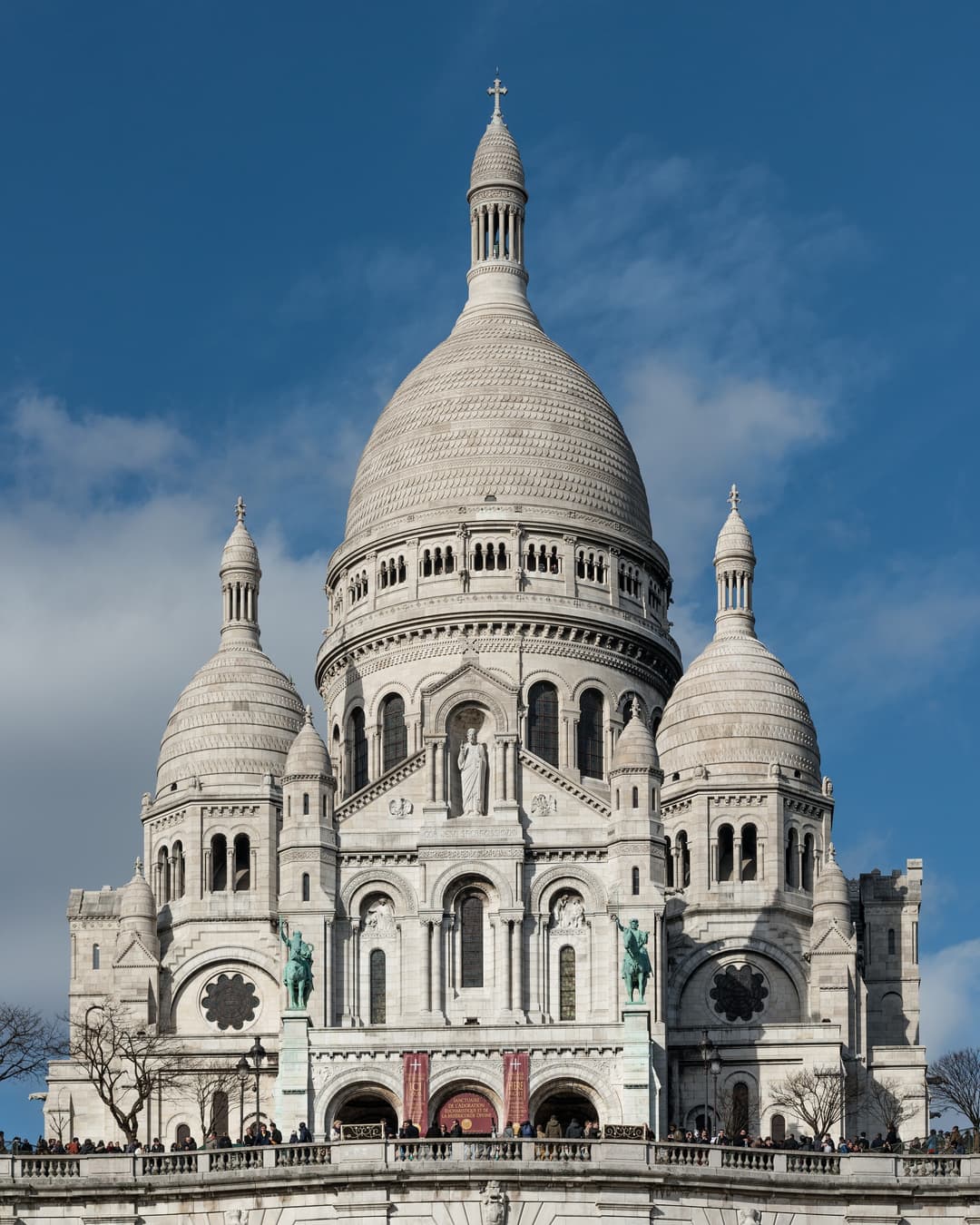 Front view of Sacré-Cœur's white domes and facade in daylight.