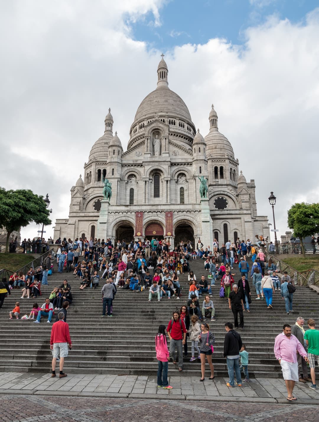 Front exterior view of Sacré-Cœur Basilica and its crowded entrance steps.