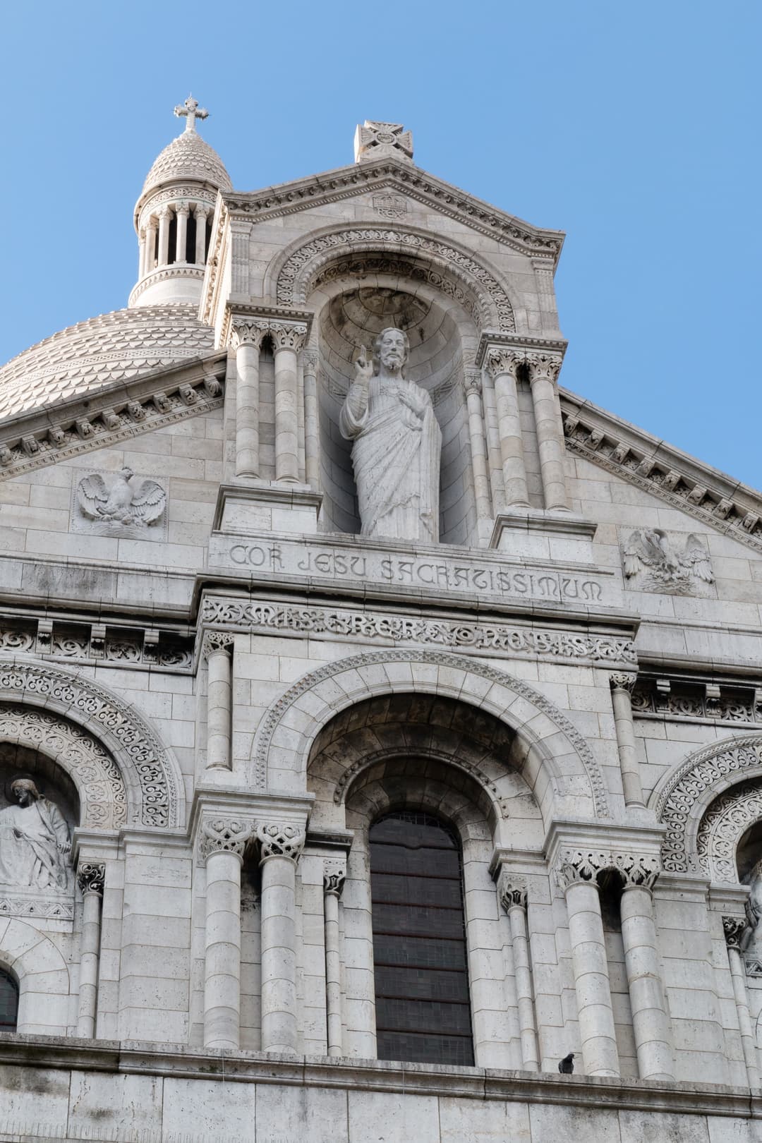 Low-angle detail of the Sacré-Cœur facade and Christ statue in daylight.